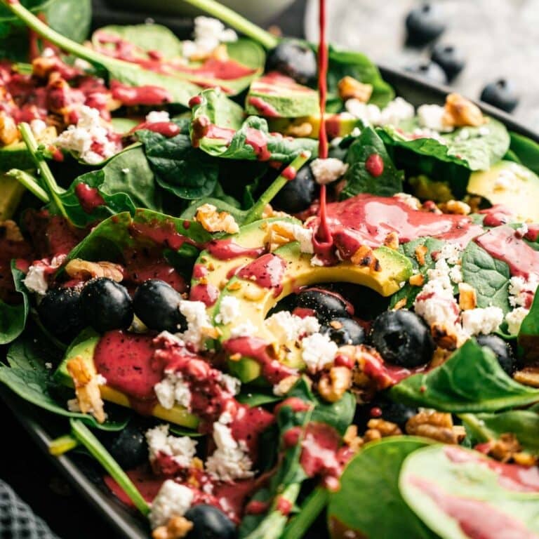 Blueberry dressing being poured over spinach and blueberry salad.