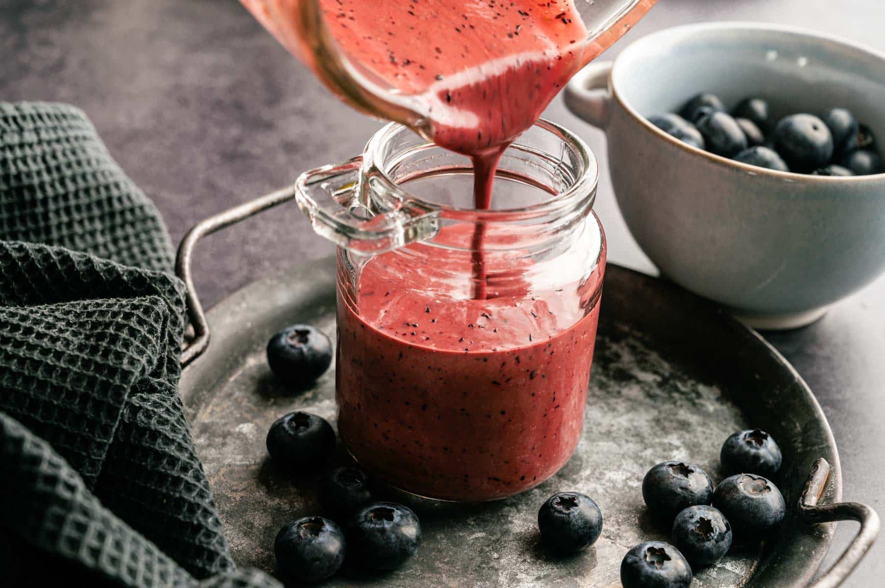 Homemade blueberry salad dressing being poured into a glasss jar.