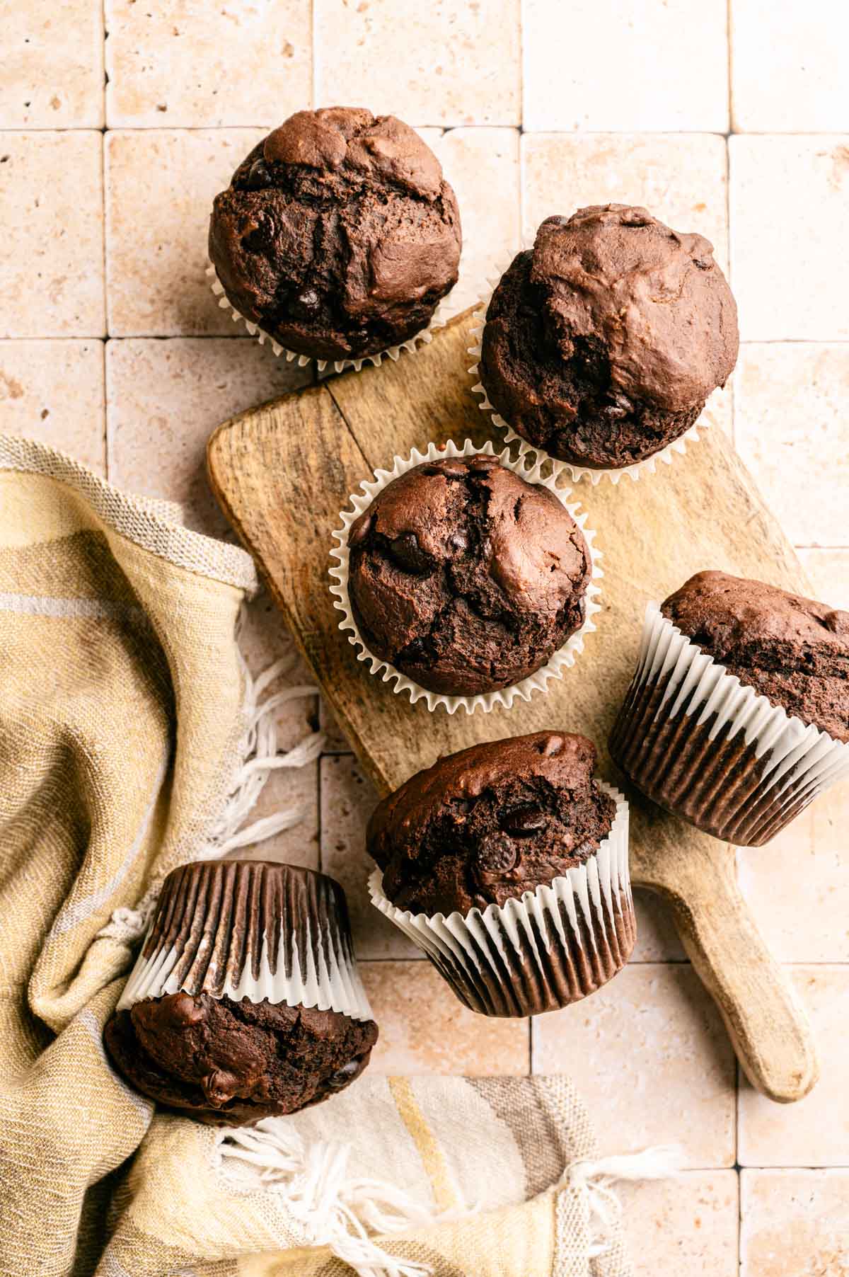 Double chocolate muffins with chocolate chips on a tiled surface.