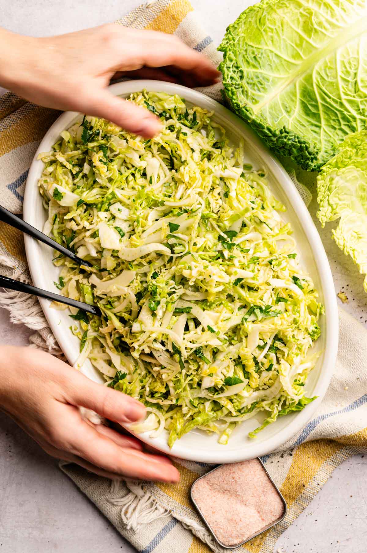 Woman reaching for an oval serving plate filled with crispy cabbage salad.
