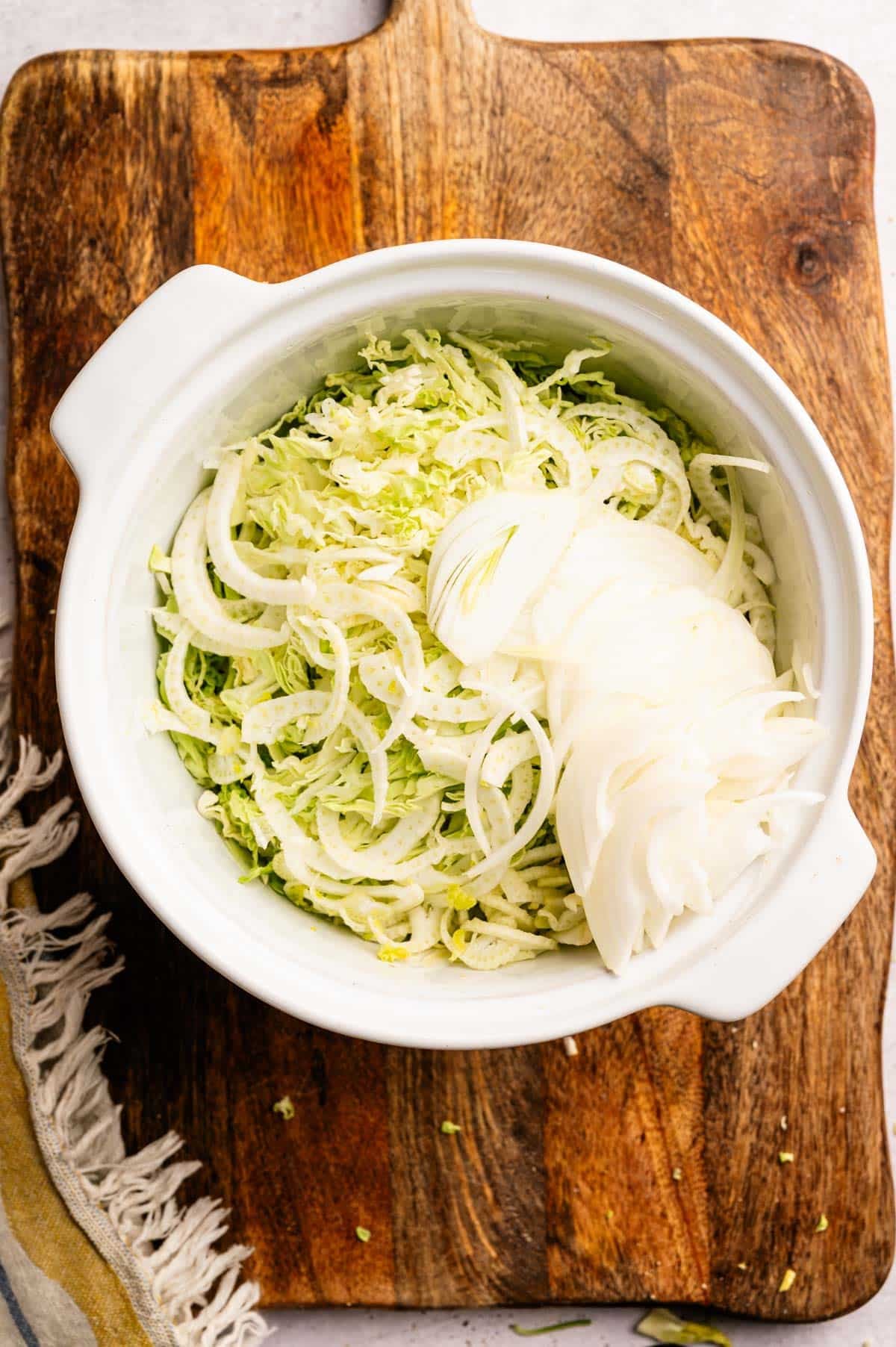 Finely shredded yellow onion in a mixing bowl with cabbage and fennel