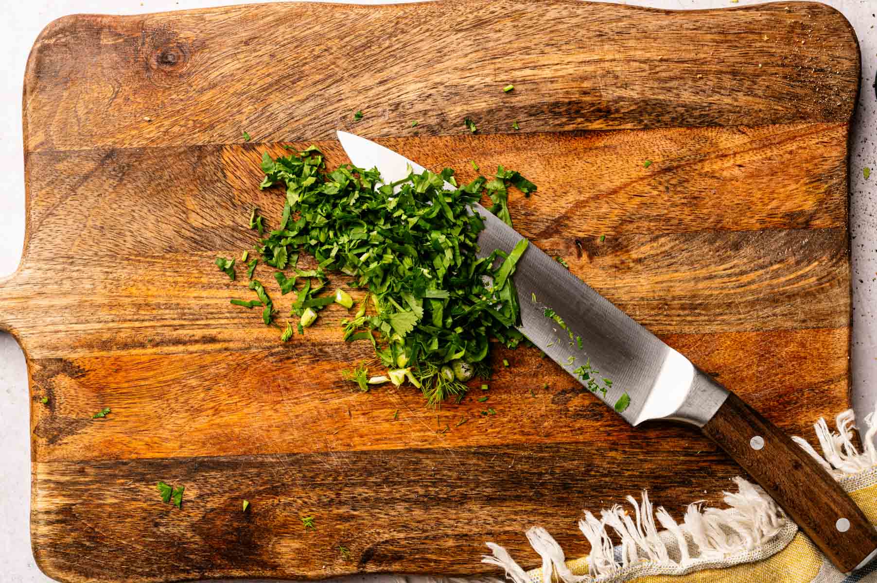 Chopped cilantro with a knife on a wooden board.