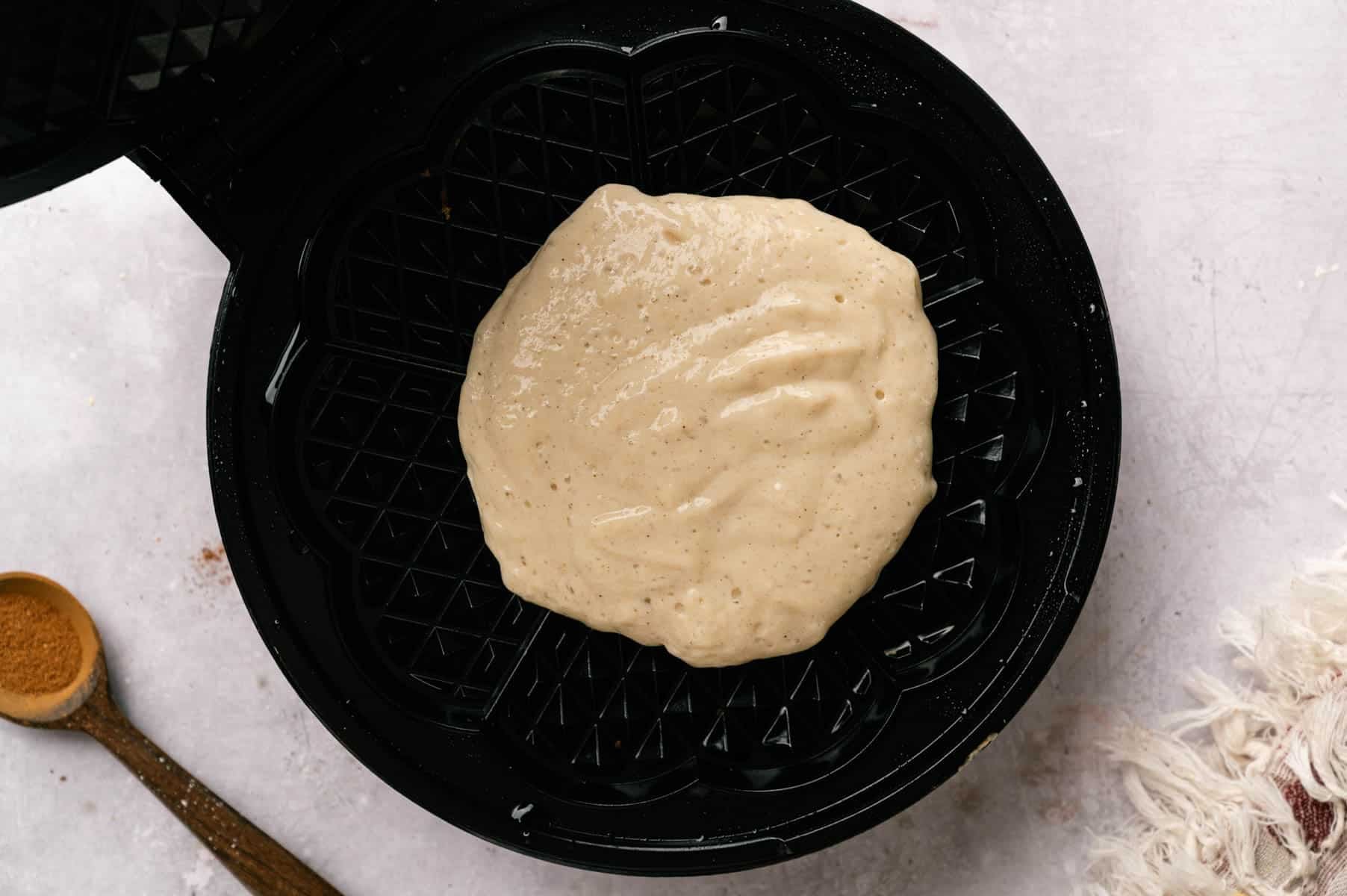 Waffle batter with protein being added to a waffle iron and being cooked.