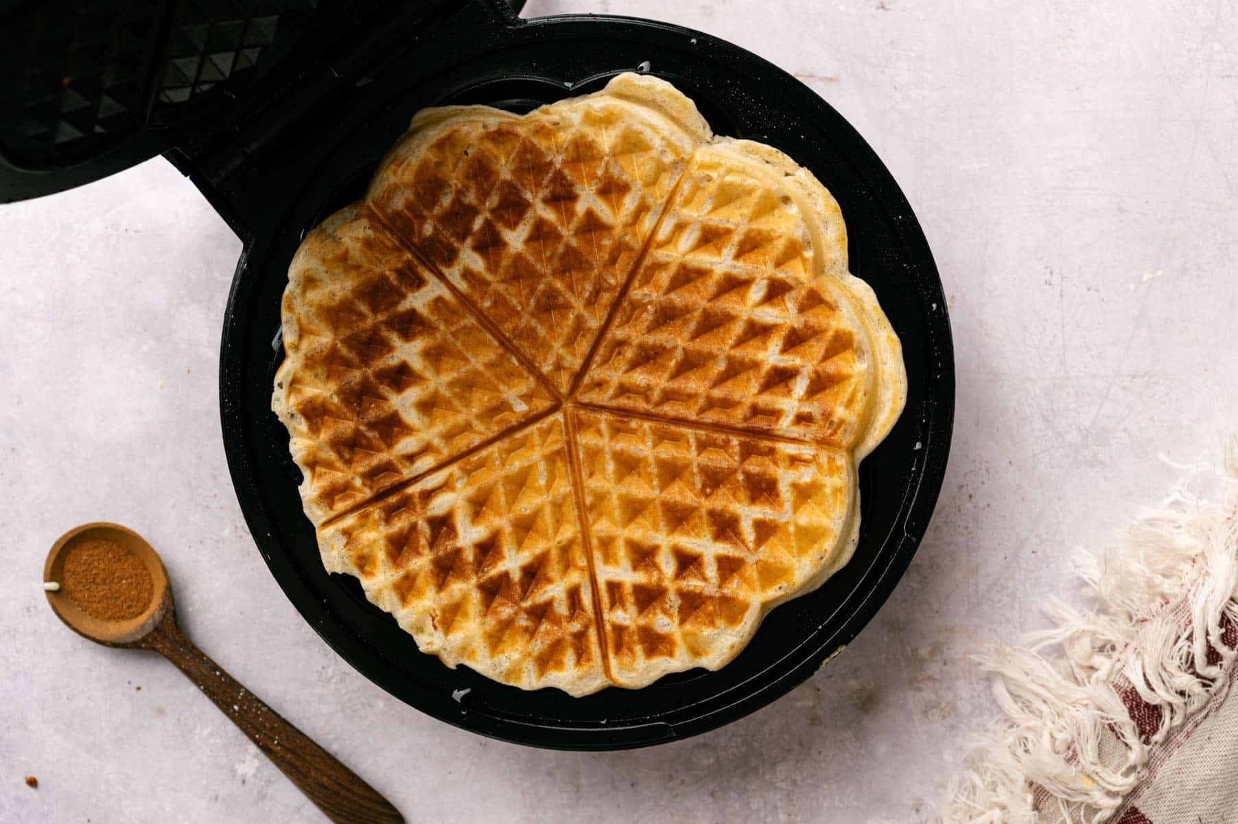 Waffle batter with protein being added to a waffle iron and being cooked.