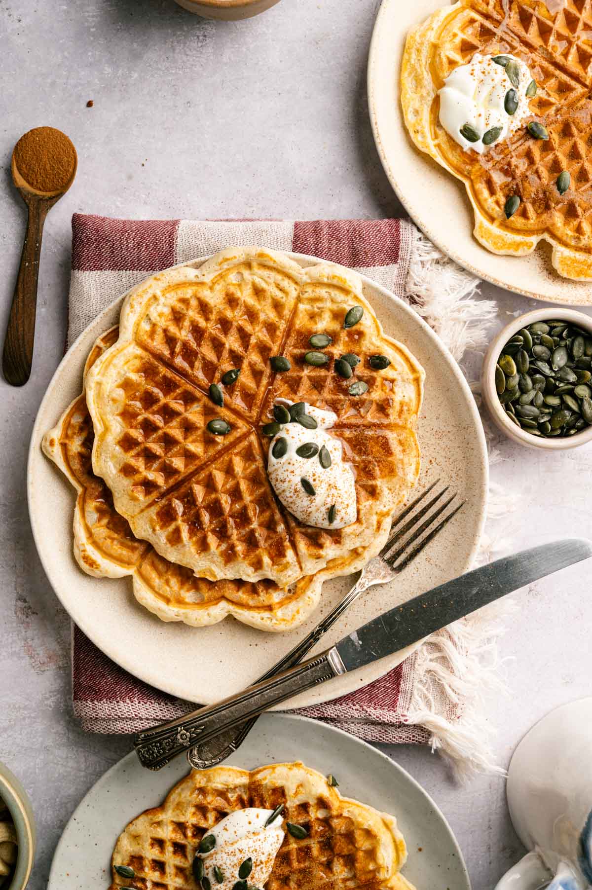 Several protein waffles on a plate with vegan whipped cream and pumpkin seeds.
