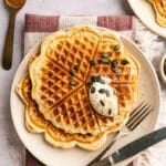 Several protein waffles on a plate with vegan whipped cream and pumpkin seeds.