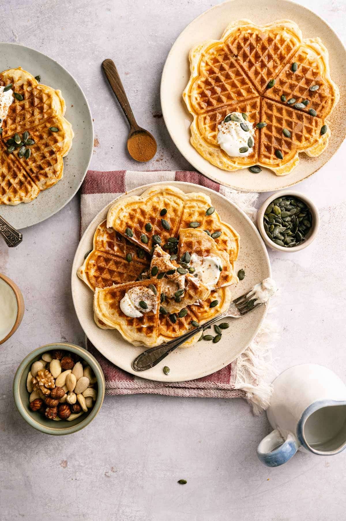 Several protein waffles on a plate with vegan whipped cream and pumpkin seeds.