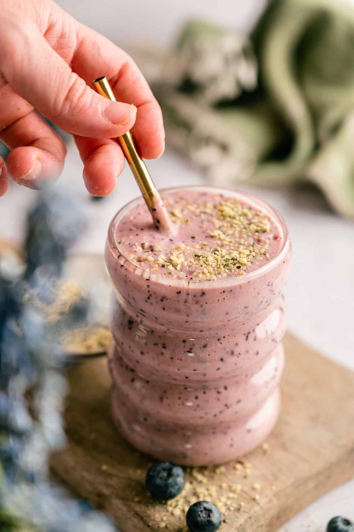 Woman mixing a blueberry and pineapple smoothie with a metal straw.