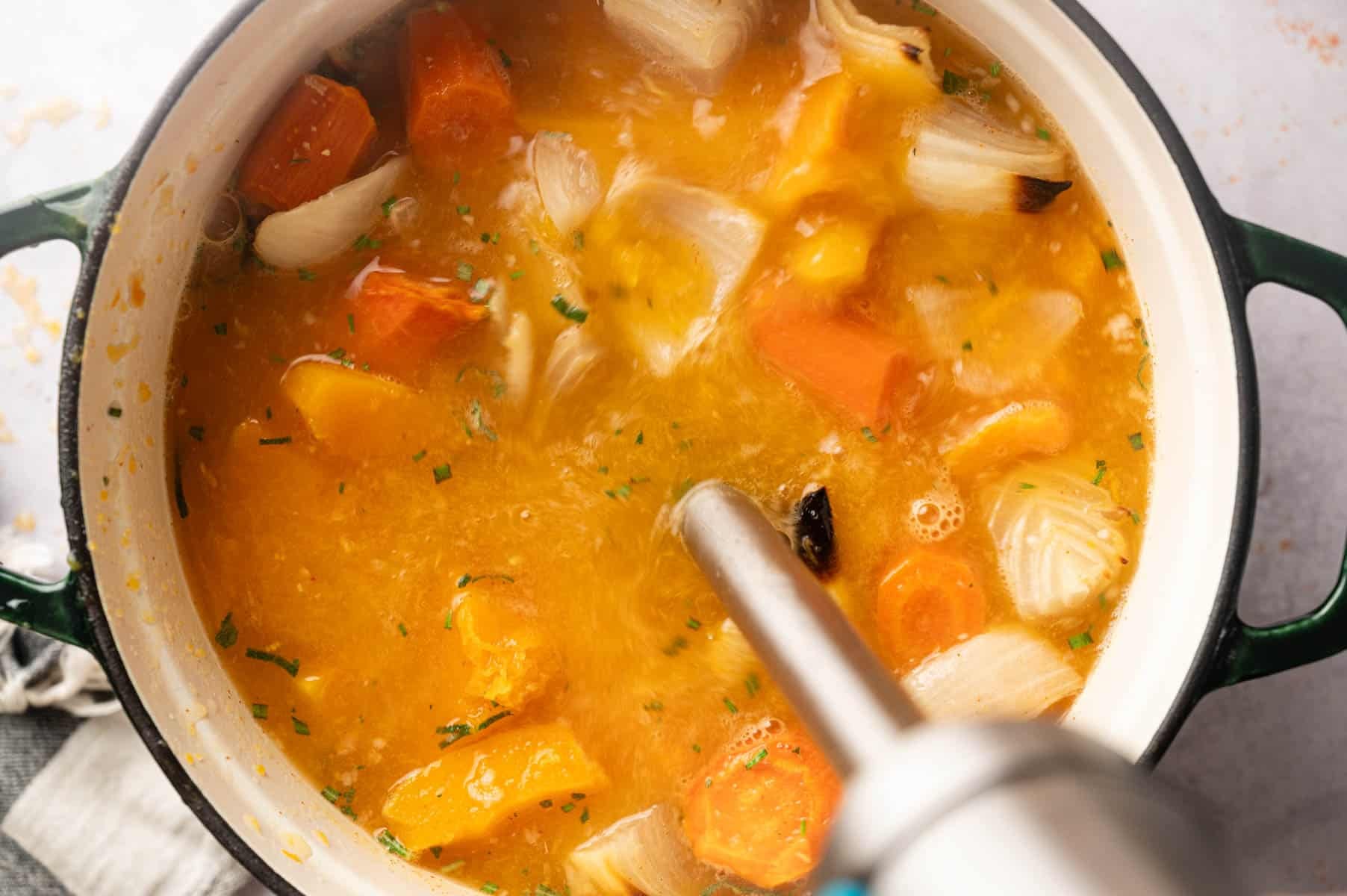Immersion blender in pot of soup blending it until cream.