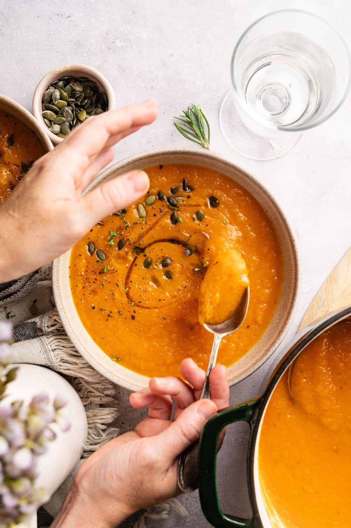 Woman reaching for a cozy bowl of carrot and butternut squash soup on a white counter.